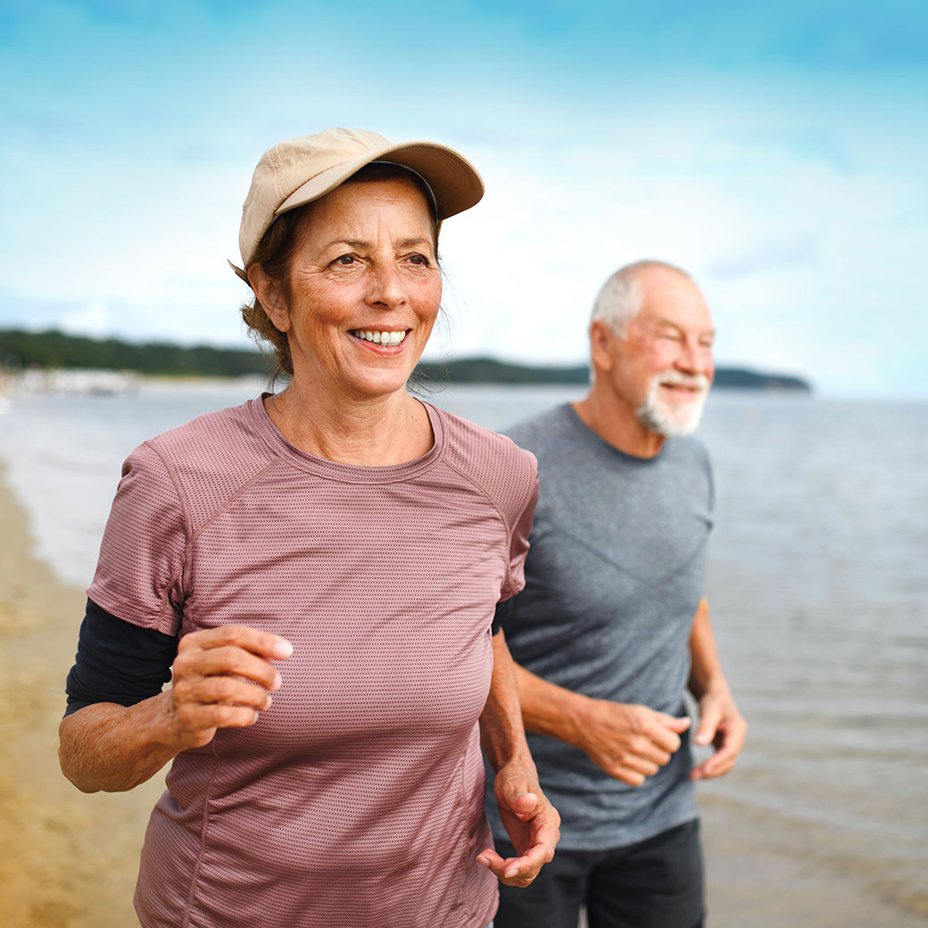 Female running on the beach with her partner behind.