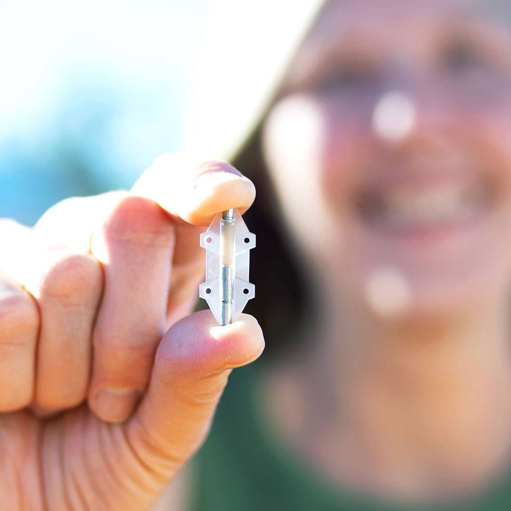 Women smiling and holding the Revi implant between her index finger and thumb.