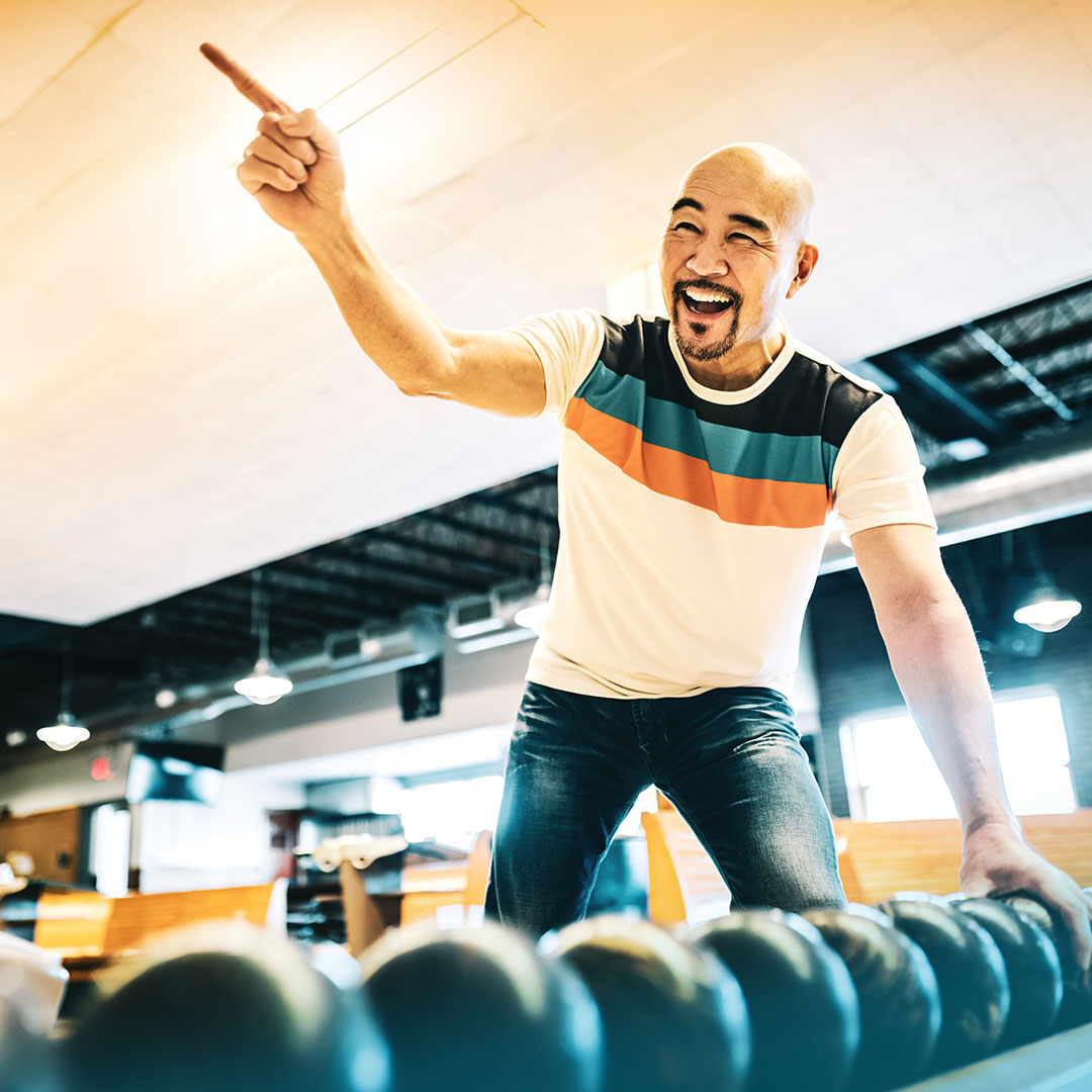 Man excited and pointing, while grabbing a bowling ball for another round.